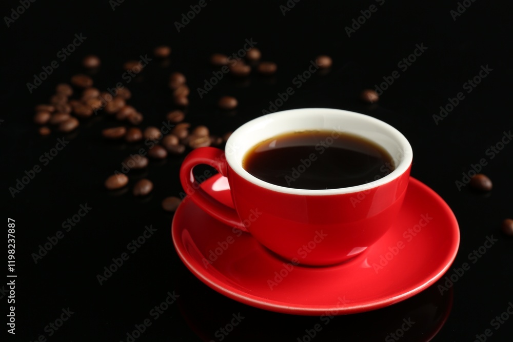 Obraz premium Red cup with coffee and roasted beans on black background, closeup