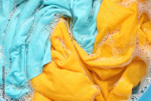 Colorful clothes soaked in water before washing, top view photo