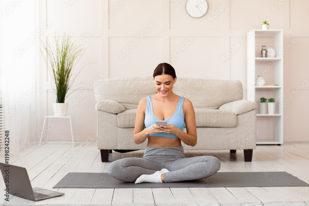 Young Woman Using Cellphone Exercising At Laptop Sitting On Gymnastic Mat At Home. Copy Space Young Woman Using Cellphone Exercising At Laptop Sitting On Gymnastic Mat At Home. Copy Space