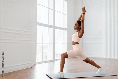 Yoga Training. Calm African American Lady Standing In 1 Warrior I Or Anjaneyasana Pose On Mat, Doing Forward Lunges Raising Arms Lifting Hands Up, Training At Home Or Fitness Studio, Free Copy Space photo