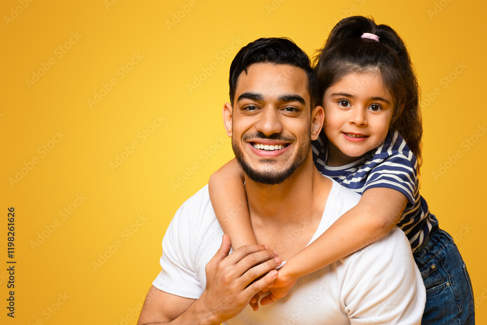 Fototapeta premium Portrait Of Happy Young Middle Eastern Dad And Cute Little Daughter Posing Together Over Yellow Background, Female Kid Embracing Daddy From The Back And Smiling At Camera, Panorama, Copy Space