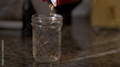Slow motion coffee beans pouring into a small glass mason jar while the morning light cracks through the window.  Early morning routine, whole bean coffee in falling and bouncing in the sun.