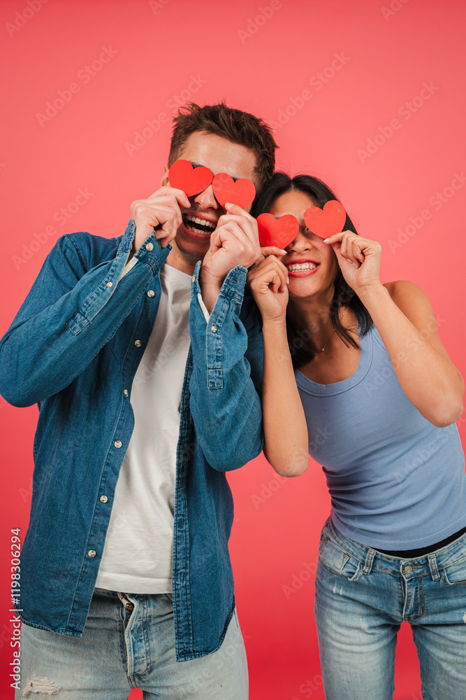 © Jose Calsina - Vertical. Playful young couple holding red heart shapes and making funny faces against a vibrant red background, celebrating love and happiness with joyful expressions in a fun and creative Valentine © Jose Calsina - Vertical. Playful young couple holding red heart shapes and making funny faces against a vibrant red background, celebrating love and happiness with joyful expressions in a fun and creative Valentine