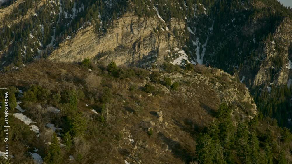 Flying around grassy rocky mountain top with patches of snow around - sunset glow Flying around grassy rocky mountain top with patches of snow around - sunset glow