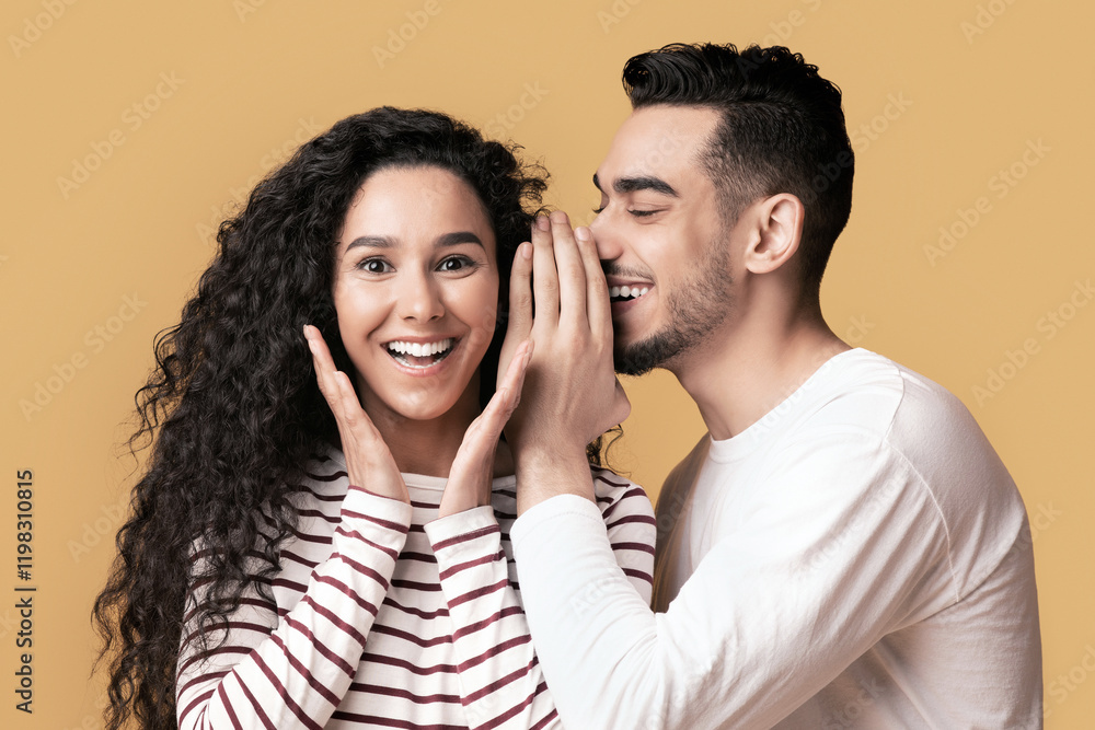 Big Secret. Young Arab Man Sharing News With His Excited Girlfriend, Surprised Middle Eastern Woman Raising Hands In Amazement While Standing Together Over Yellow Studio Background, Free Space