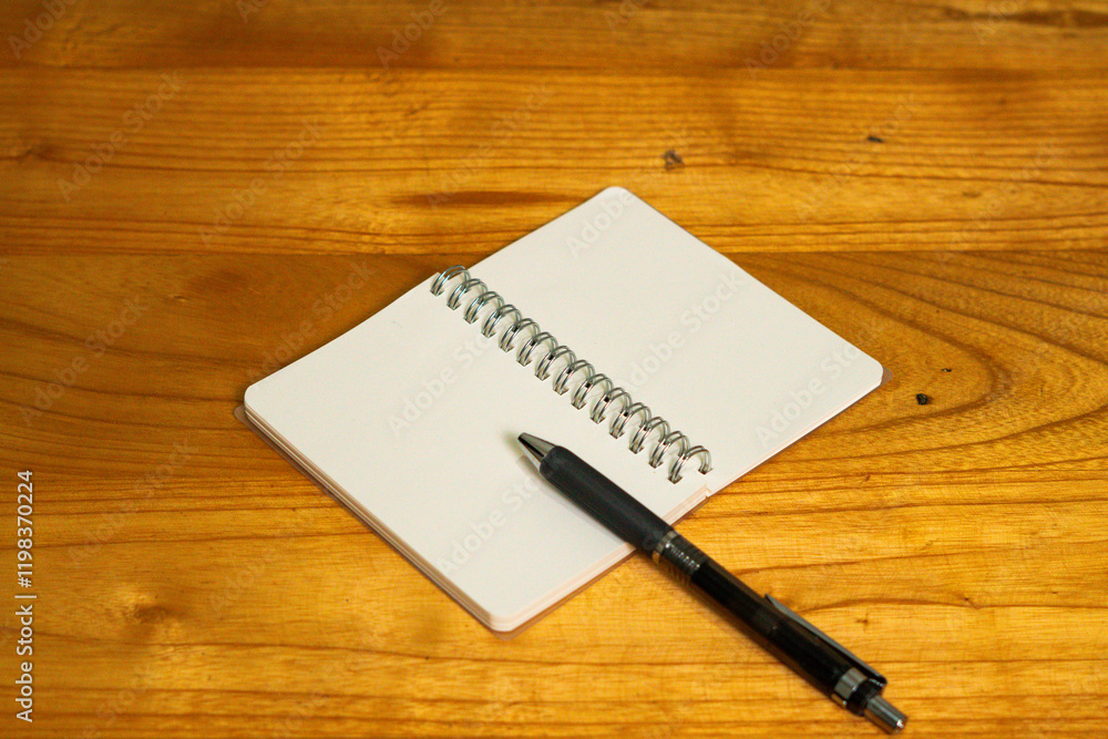An open spiral notebook with blank pages and a black pen placed on a wooden desk. Perfect for themes of writing, planning, journaling, or creativity An open spiral notebook with blank pages and a black pen placed on a wooden desk. Perfect for themes of writing, planning, journaling, or creativity