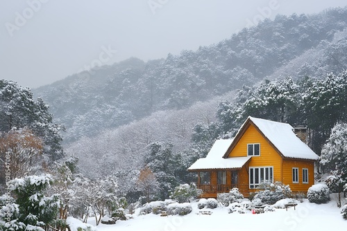 A charming yellow cabin sits amidst a snow-covered mountain forest, offering a peaceful winter escape.
