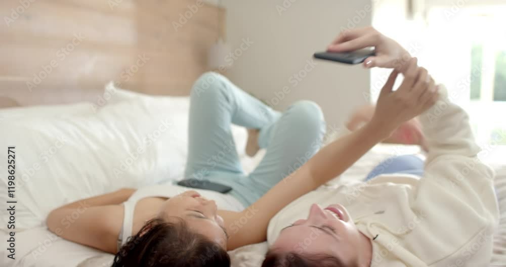 Taking selfie, two diverse women friends lying on bed and smiling at home Taking selfie, two diverse women friends lying on bed and smiling at home