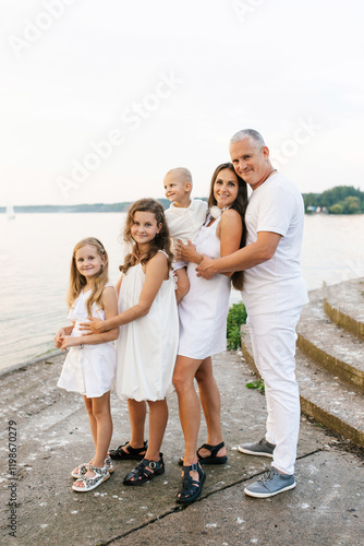 Happy family of five, including couple and three children are posing for a photo on pier by the water