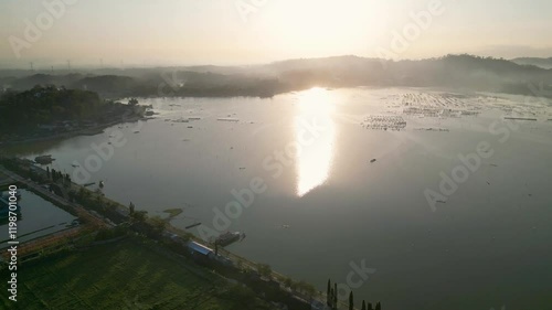 A beautiful sunrise bathes Rawa Jombor in warm golden light, with the tranquil lake reflecting the colors and majestic mountains providing a breathtaking backdrop. photo