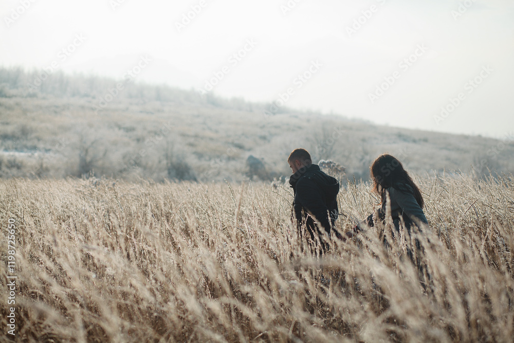 two people walking through a field of tall grass. They are in the center of the frame, and their figures are visible from the back. two people walking through a field of tall grass. They are in the center of the frame, and their figures are visible from the back.