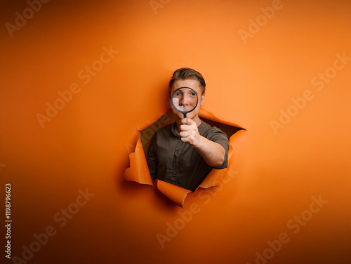 A young person peers through a magnifying glass from a hole in an orange background, creating a playful, inquisitive scene.