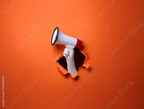 A hand bursts through an orange background, holding a megaphone.  The scene conveys a powerful message or announcement. photo