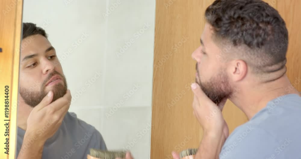 Grooming beard, man using brush and looking in mirror in bathroom Grooming beard, man using brush and looking in mirror in bathroom