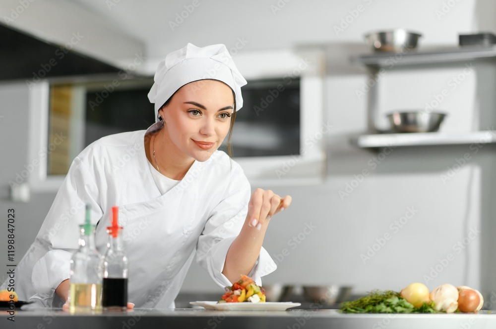 young beautiful smiling woman chef wearing in white suit at kitchen. Blurred background young beautiful smiling woman chef wearing in white suit at kitchen. Blurred background
