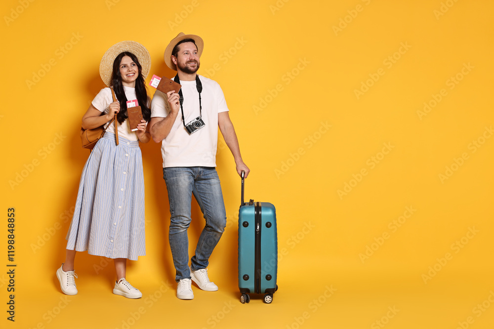 Tourism. Happy couple in hats with suitcase, passports and tickets on yellow background, space for text Tourism. Happy couple in hats with suitcase, passports and tickets on yellow background, space for text