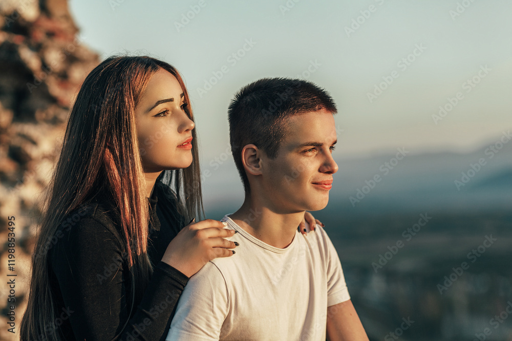 the couple looks in one direction, into the distance, and looks thoughtful. In the background is a blurry landscape with mountains and sky. the couple looks in one direction, into the distance, and looks thoughtful. In the background is a blurry landscape with mountains and sky.