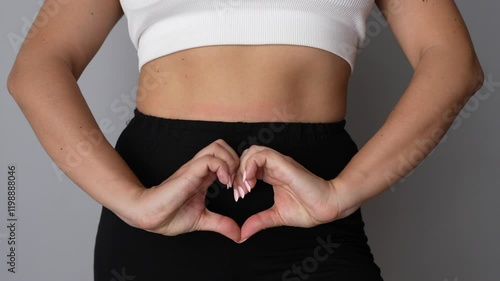 Young woman forming heart shape with her hands on lower abdomen on a grey background. Health care, genicological concept photo