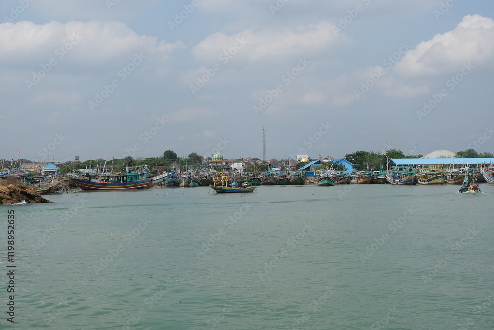 Fototapeta premium Scenic View of Traditional Wooden Boats Docked at a Bustling Coastal Harbor Under a Blue Sky