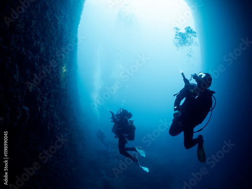 Wallpaper Mural silhouette of unrecognizable scuba divers with flashlights swimming in narrow dark cave with rough rocky formations undersea in deep clear water, concept of active leisure and underwater adventure Torontodigital.ca