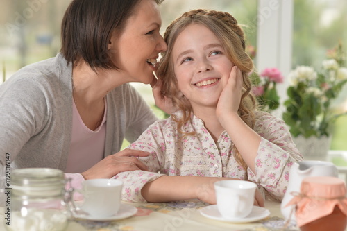 Happy mom and daughter drinking tea at home