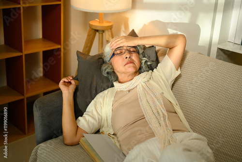 Obraz na plátně Sick senior woman lying on sofa with hand on her forehead appearing fatigued or