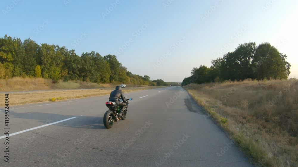 Follow to motorcyclist in helmet riding on sport motorbike at highway. Man racing his motorcycle on autumnal country road. Guy driving bike during trip. Concept of freedom and adventure. Aerial shot Follow to motorcyclist in helmet riding on sport motorbike at highway. Man racing his motorcycle on autumnal country road. Guy driving bike during trip. Concept of freedom and adventure. Aerial shot