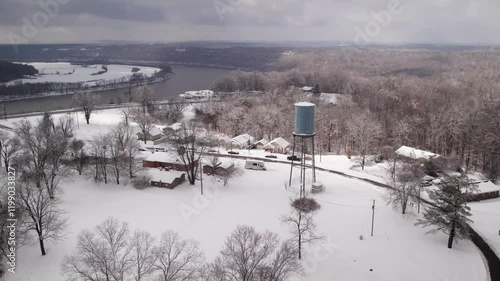 view of water tower standing in snow-covered area with leafless trees, and a river in the background photo