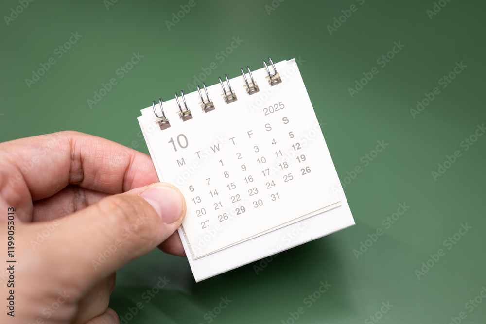 Fototapeta premium Hand holding mini calendar for 2025 OCTOBER background. Calendar concept with 2025 OCT calendar.