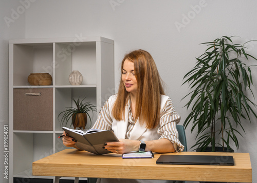 Smiling young woman home working table. There laptop on table, girl taking notes in notebook, planning her tasks with concentration. Concept: remote work, education, planning and personal efficienc photo