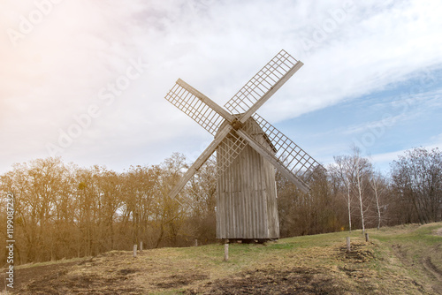 A traditional wooden windmill in a rural landscape under a blue sky with soft sunlight. Perfect for themes of heritage, countryside, or historical architecture. photo