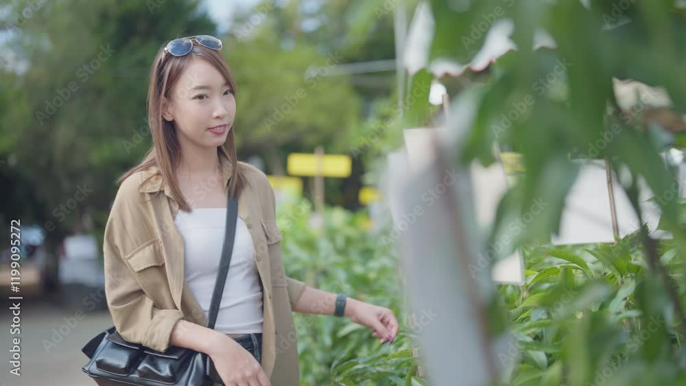 A woman is shopping for plants in a garden. She is wearing a brown jacket and a white shirt A woman is shopping for plants in a garden. She is wearing a brown jacket and a white shirt