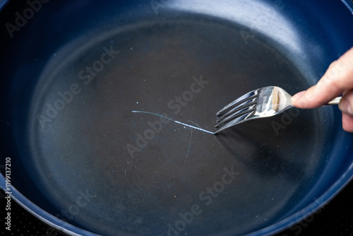 Fork scratching the non stick coating on a frying pan