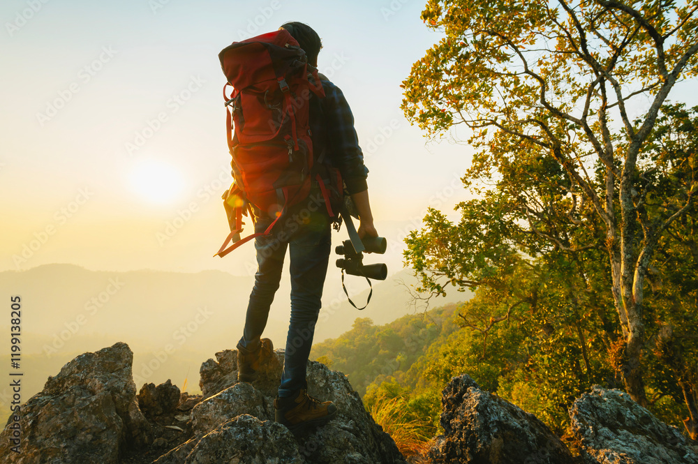 Fototapeta premium man with a backpack is standing on a mountain top, looking out at the sunset
