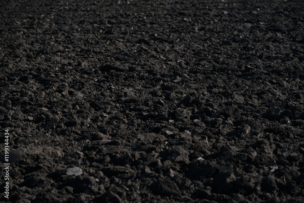 Dark soil lies freshly turned in a rural landscape as dusk settles. The rich earth reveals small stones and texture, indicating readiness for planting. Freshly plowed field. Close up Dark soil lies freshly turned in a rural landscape as dusk settles. The rich earth reveals small stones and texture, indicating readiness for planting. Freshly plowed field. Close up