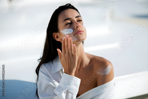 Beautiful woman applying sunscreen lotion on face and shoulder photo