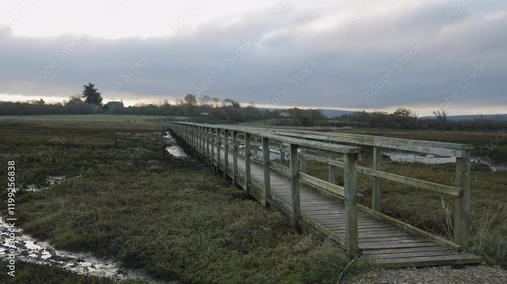 A bridge over a muddy field with a cloudy sky in the background. The bridge is wooden and he is old A bridge over a muddy field with a cloudy sky in the background. The bridge is wooden and he is old