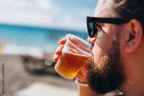 Man drinks beer on beach from plastic glass, alcoholism, drinking alcohol photo