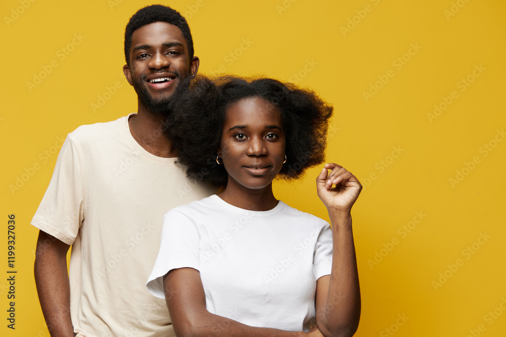 Fototapeta premium Two young Black adults smiling in front of a bright yellow background, showcasing friendship and joy in casual attire with natural hairstyles