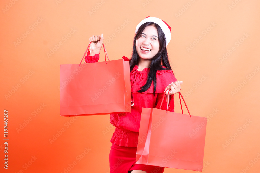 Fototapeta premium young girl standing happy candid both hands holding red bag of christmas gifts up and down, wearing red blouse and santa hat, isolated on white background