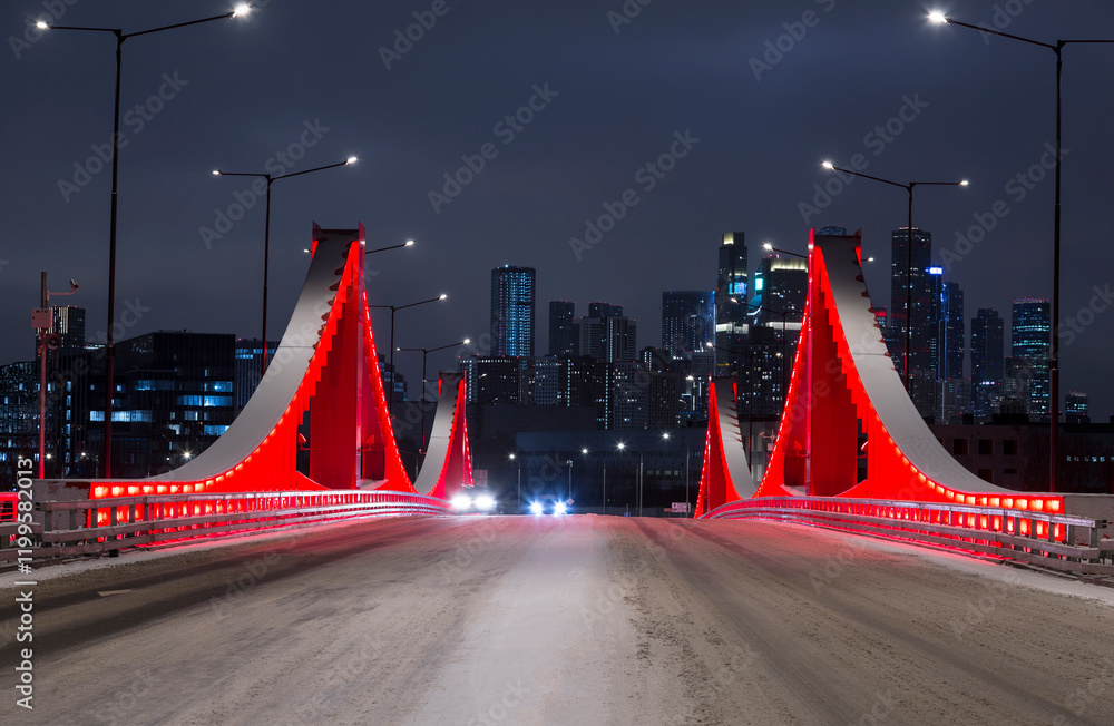 New red bridge across the Moskva River connecting the Mnyovnikovskaya and Filyovskaya floodplains with evening illumination. Moscow, Russia