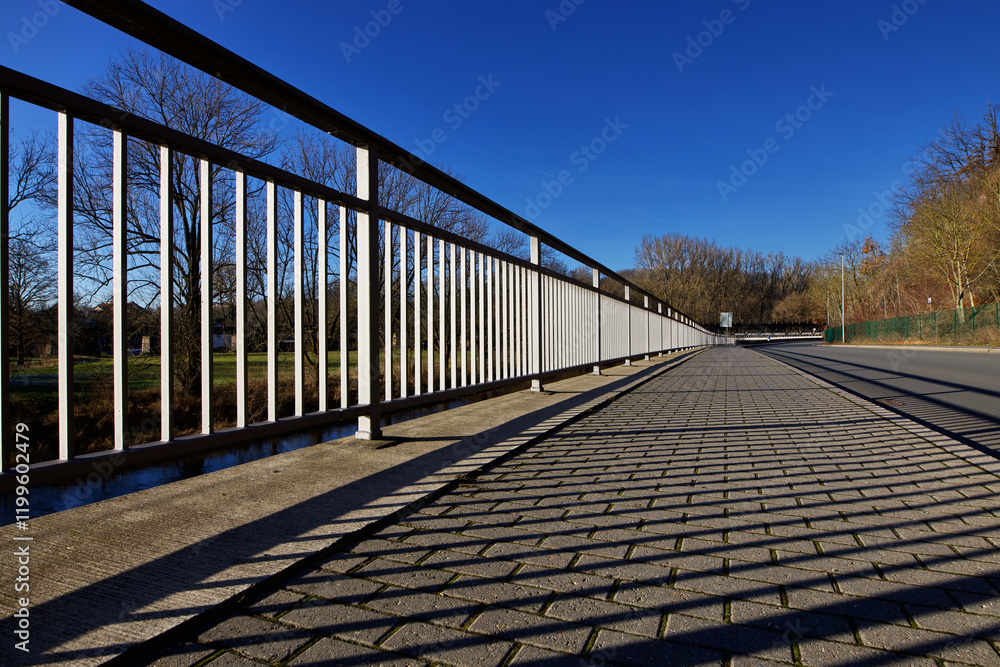 Brückengeländer im Sonnenlicht an Strasse mit Bäumen, Licht und Schatten, markante Form Design, blauer Himmel Blickwinkel von vorn, ruhige Szene in Europa Deutschland Thüringen Gera Brückengeländer im Sonnenlicht an Strasse mit Bäumen, Licht und Schatten, markante Form Design, blauer Himmel Blickwinkel von vorn, ruhige Szene in Europa Deutschland Thüringen Gera