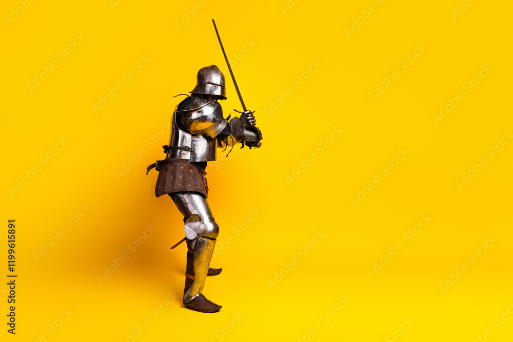 Medieval Knight in Steel Armor Posing with Sword Against Vibrant Yellow Background Medieval Knight in Steel Armor Posing with Sword Against Vibrant Yellow Background