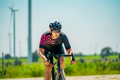 Cyclist riding on an open road near wind turbines under a clear blue sky