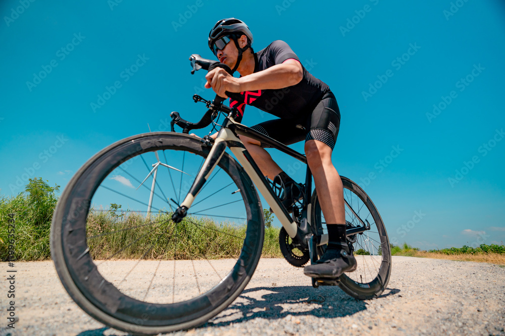 Fototapeta premium Cyclist navigating a gravel path near wind turbines under a clear blue sky