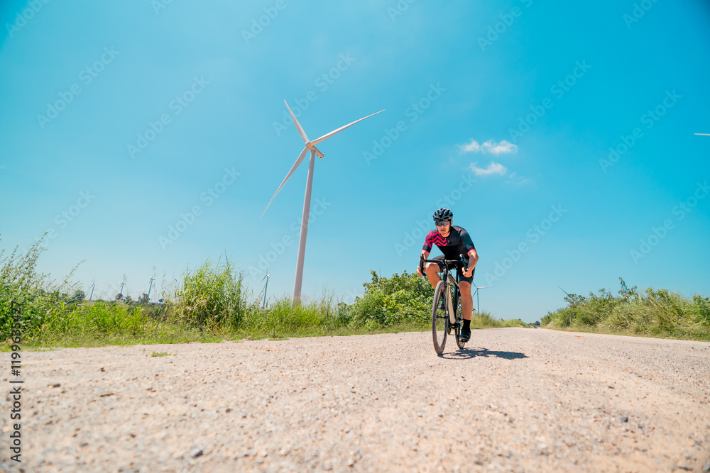 Obraz premium Cyclist navigating a gravel path with wind turbines in the background during a sunny day