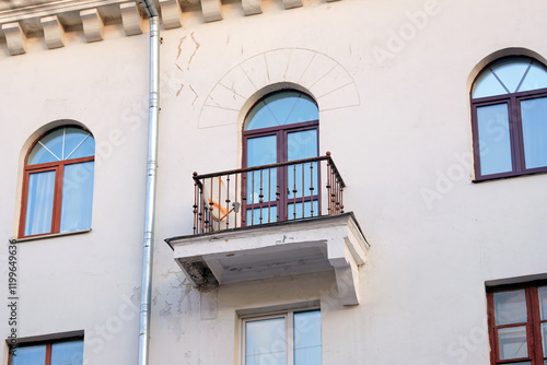 Damaged balcony support bracket and cracked plaster on the facade of residential building, requiring restoration and repair work. Unsafe building facade with cracked and broken plaster