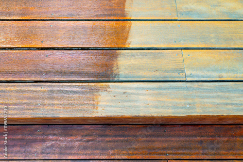 Close-up of a wooden deck showing the process of restoration with a half-stained surface contrasting weathered and treated wood during a home improvement project. photo