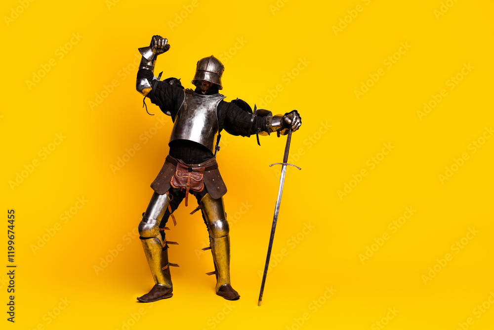 Young man dressed in medieval knight's armor striking a heroic pose against a vibrant yellow background Young man dressed in medieval knight's armor striking a heroic pose against a vibrant yellow background