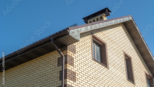 A newly built two-storey house, the walls of which are lined with decorative bricks. Brickwork. A chimney for a fireplace on the roof of the house.